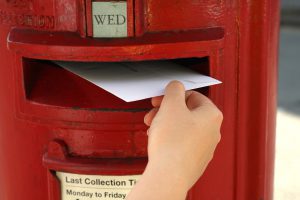 posting a letter to red british postbox on street